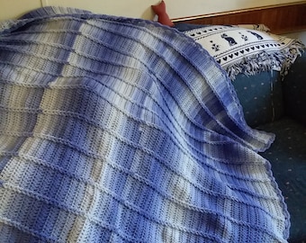 Könnte beinhalten: Eine gehäkelte Wolldecke in Blautönen und Weiß. Die Decke ist mit einem einfachen Stichmuster gearbeitet und hat einen gewellten Rand.