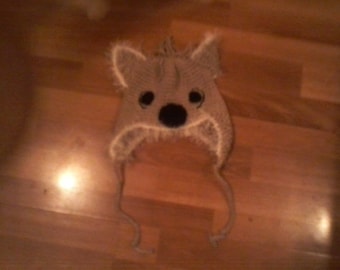 May include: A brown and white knitted hat shaped like a koala with black eyes and a black nose.