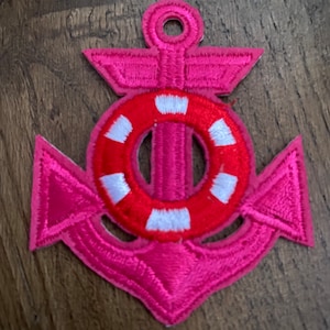 May include: A pink and red embroidered anchor with a white life preserver design. The anchor is a nautical themed patch.