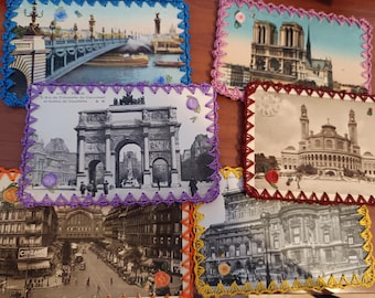 May include: A collection of six vintage postcards featuring black and white or sepia architectural scenes of Paris, each bordered with hand-crocheted yarn in vibrant colors including blue, purple, red, orange, and yellow, with small floral accents.