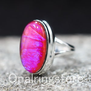 Puede incluir: Un anillo de plata con una gran piedra de ópalo rosa ovalada. El anillo tiene una banda simple con un acabado texturizado.