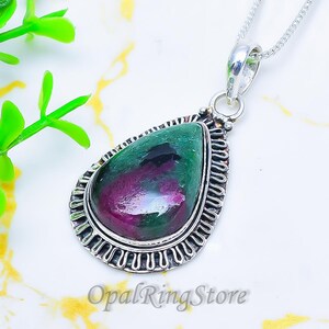Puede incluir: Collar con colgante en forma de lágrima con una piedra preciosa verde y magenta. La piedra está engastada en un marco plateado ornamentado y cuelga de una fina cadena de plata. El logotipo de OpalRingStore es visible.