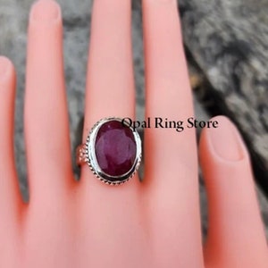 May include: A silver ring featuring a large oval ruby gemstone. The ring has a decorative border around the stone.