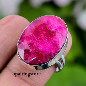 May include: A silver ring with a large, oval-shaped, pink ruby gemstone. The ring is set in a simple, silver band.