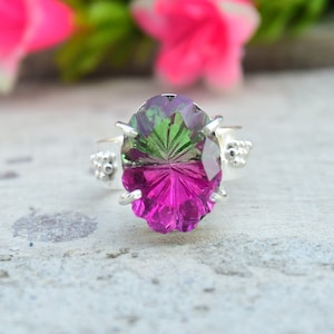 Puede incluir: Un anillo de plata con una gran piedra ovalada de color verde y rosa. La piedra preciosa está facetada y tiene un patrón de estrella.