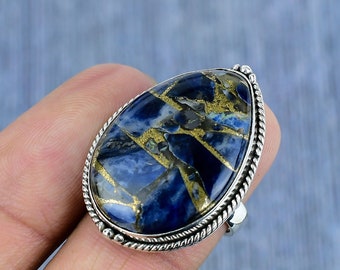 May include: A silver ring featuring a large, teardrop-shaped stone. The stone has a striking blue base color with gold and black veining. The ring's setting has a detailed, rope-like border.