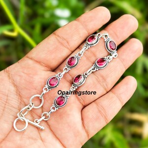 May include: A silver bracelet with a toggle clasp features a chain with oval-shaped pink gemstones set in silver.