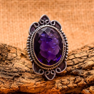 May include: A silver ring featuring an oval amethyst gemstone set in an intricate ornate design.