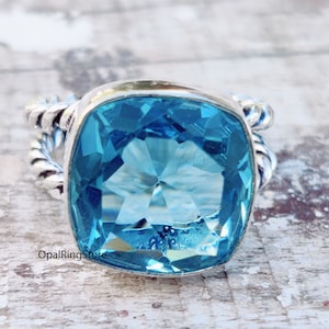 May include: A silver ring with a large, square-shaped, light blue gemstone. The ring has a twisted band.