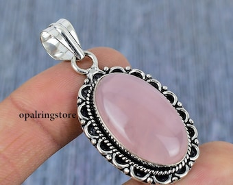 May include: A silver pendant with a delicate, ornate design features a large, oval-shaped, pale pink rose quartz gemstone.