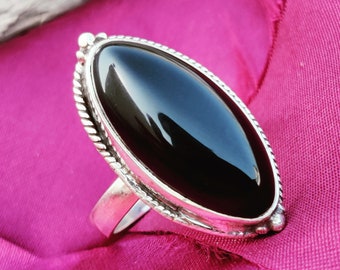 May include: A silver ring featuring a large, oval-shaped black onyx gemstone. The ring has a detailed, textured band.
