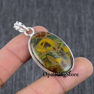 May include: Oval-shaped pendant with a silver setting and a colourful, patterned stone. The stone features shades of brown, yellow, and green.