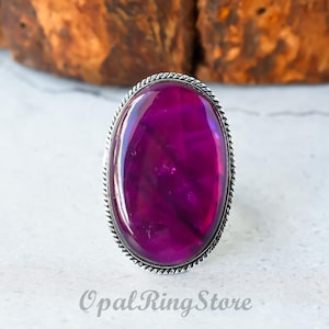 May include: A silver ring with a large oval-shaped purple gemstone set in a silver bezel. The ring has a rope-like design around the edge of the bezel.