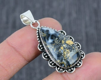 May include: A silver pendant featuring a teardrop-shaped black and white opal with yellow accents. The pendant has a decorative silver border with small beads.