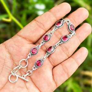 May include: A silver bracelet with a toggle clasp features six oval-shaped pink gemstones set in silver.