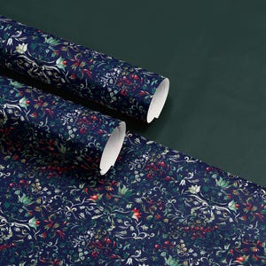 K&ouml;nnte beinhalten: Rollen von marineblauem Tapetenpapier mit floralem Muster und roten, gr&uuml;nen und wei&szlig;en Akzenten. Die Tapete ist auf einer dunkelgr&uuml;nen Oberfl&auml;che ausgerollt und zeigt das komplizierte Design. Die Rollen sind teilweise ausgerollt und zeigen die wei&szlig;e R&uuml;ckseite.