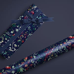 K&ouml;nnte beinhalten: Eine marineblaue Geschenkbox, verpackt in floral gemustertem Papier mit passendem Samtband. Eine Rolle des gleichen floral gemusterten Papiers ist ebenfalls vorhanden. Das Blumenmuster enth&auml;lt rote, gr&uuml;ne und wei&szlig;e Akzente.