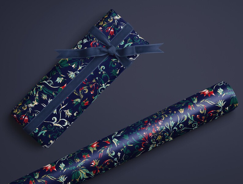 K&ouml;nnte beinhalten: Eine marineblaue Geschenkbox, verpackt in floral gemustertem Papier mit passendem Samtband. Eine Rolle des gleichen floral gemusterten Papiers ist ebenfalls vorhanden. Das Blumenmuster enth&auml;lt rote, gr&uuml;ne und wei&szlig;e Akzente.