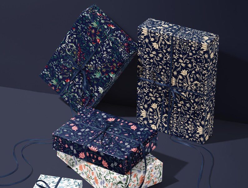 K&ouml;nnte beinhalten: Mehrere Geschenkboxen, verpackt in gemustertem Papier mit floralen Designs in Marineblau, Creme und Rot. Jede Box ist mit einem marineblauen Band gebunden. Die Boxen sind gestapelt und auf einer dunkelblauen Oberfl&auml;che angeordnet.