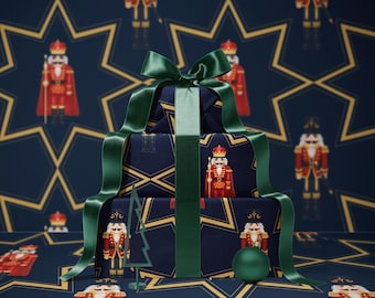 May include: A stack of wrapped gifts with a dark blue background featuring a gold star and nutcracker pattern. The gifts are tied with a green satin ribbon and bow. A green Christmas ornament and a green tree-shaped decoration are also present.