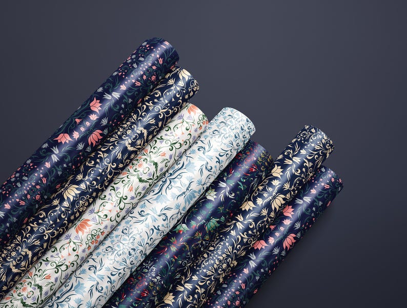 K&ouml;nnte beinhalten: Mehrere Rollen Geschenkpapier mit floralen Mustern in verschiedenen Farben, darunter Marineblau, Wei&szlig; und Rosa. Das Papier zeigt ein sich wiederholendes botanisches Design mit Blumen und Bl&auml;ttern. Die Rollen sind diagonal vor dunklem Hintergrund angeordnet.