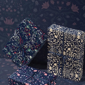 K&ouml;nnte beinhalten: Drei Geschenkboxen, verpackt in Papier mit floralen Mustern. Die Boxen sind mit dunkelblauen B&auml;ndern gebunden. Der Hintergrund ist ein dunkelblaues Blumenmuster.