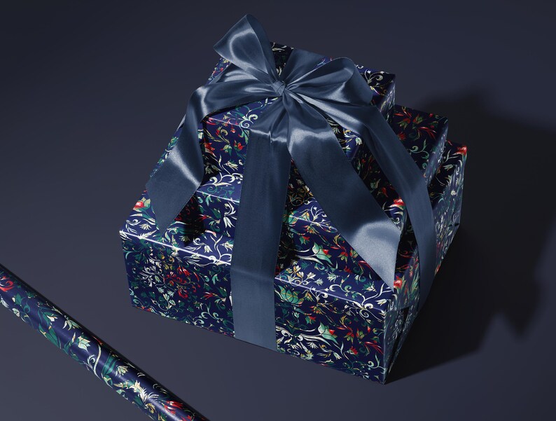 K&ouml;nnte beinhalten: Drei gestapelte Geschenkboxen, verpackt in marineblauem Papier mit einem floralen Muster in Rot, Gr&uuml;n und Wei&szlig;. Eine gro&szlig;e marineblaue Satinschleife ist oben gebunden. Eine Rolle passenden Geschenkpapieres ist zu sehen.