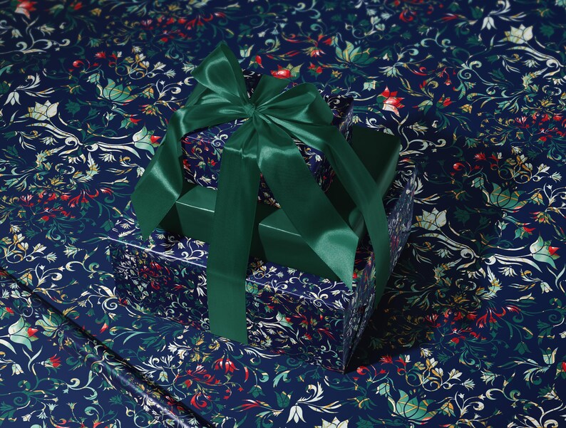 K&ouml;nnte beinhalten: Ein Geschenkbox-Set mit einem dunkelblauen floralen Muster, gekr&ouml;nt von einer gro&szlig;en smaragdgr&uuml;nen Satinschleife. Die Boxen liegen auf passendem floralem Geschenkpapier, was eine zusammenh&auml;ngende und elegante Pr&auml;sentation ergibt.