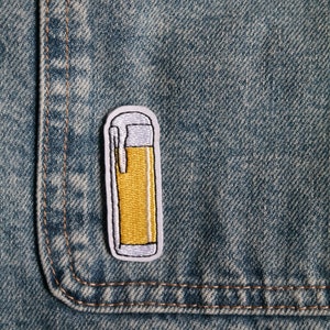 Könnte beinhalten: Ein gestickter Aufnäher eines Feuerzeugs in Gelb und Weiß, der auf eine blaue Jeansjacke genäht ist.