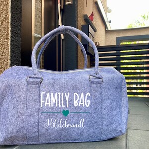 Può includere: Una borsa da viaggio in feltro grigia con il testo "FAMILY BAG Hildebrandt" e un cuore verde.