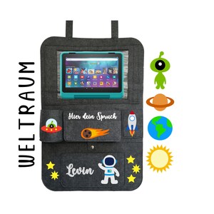 May include: A gray felt car seat organizer with a clear plastic window for a tablet. It has pockets for storage and features a space-themed design with a rocket, stars, a comet, a planet, an alien, and a sun. The text "Hier dein Spruch" and "Levin" is embroidered on the organizer.