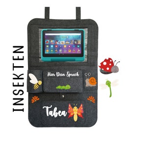 May include: Gray felt car seat organizer with a clear plastic window for a tablet. The organizer has pockets for storage and features embroidered insects, a caterpillar, and the name "Tabea".
