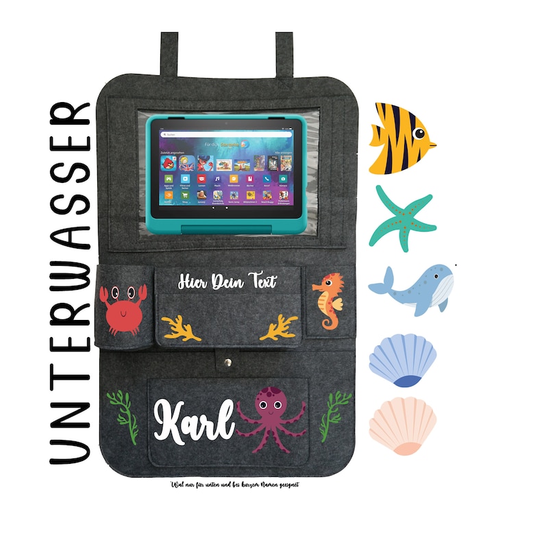 May include: Gray felt tablet holder with a clear plastic window for a tablet. The holder has pockets on the sides and a pocket on the bottom. The pockets are decorated with sea creatures, including a crab, a seahorse, an octopus, a starfish, a whale, and a fish. The text "Hier Dein Text" is printed on the holder. The text "Karl" is printed on the bottom pocket. The text "Ideal f&uuml;r Auto und f&uuml;r zu Hause. Montage m&ouml;glich" is printed on the bottom of the holder.