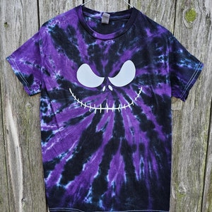 Może przedstawiać: Koszulka tie-dye w kolorze fioletowym i czarnym z białym nadrukiem twarzy Jacka Skellingtona.