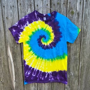 Op de afbeelding: Een tie-dye T-shirt met een draaiende print in tinten paars, blauw, geel en groen.