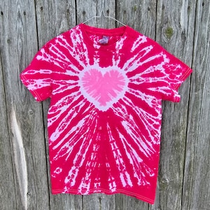 Puede incluir: Una camiseta tie-dye rosa y blanca con un diseño de corazón en el centro.