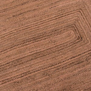 Op de afbeelding: Close-up van een rechthoekig bruin jute vloerkleed met een geweven ontwerp. Het vloerkleed heeft een centraal rechthoekig patroon met concentrische randen. De natuurlijke vezels cre&euml;ren een textuuroppervlak.
