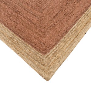 Op de afbeelding: Close-up van een geweven vloerkleed met een natuurlijke jute rand en een middenstuk in een roodbruine tint. De textuur van het vloerkleed is zichtbaar en toont de natuurlijke vezels en het geometrische ontwerp.