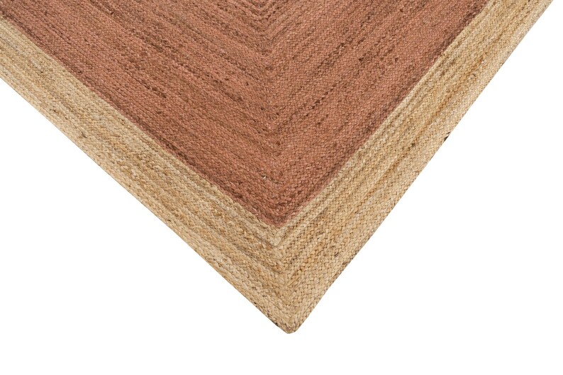 Op de afbeelding: Close-up van een geweven vloerkleed met een natuurlijke jute rand en een middenstuk in een roodbruine tint. De textuur van het vloerkleed is zichtbaar en toont de natuurlijke vezels en het geometrische ontwerp.