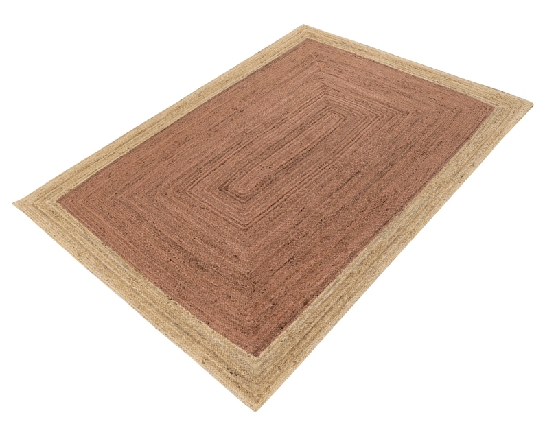 Op de afbeelding: Rechthoekig jute vloerkleed met een natuurlijke beige rand en een middenstuk in een roodbruine tint. Het vloerkleed heeft een geometrisch ontwerp met een reeks concentrische rechthoeken. Het vloerkleed is gemaakt van geweven jutevezels.