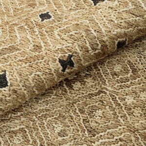 Puede incluir: Primer plano de una alfombra tejida con un patrón geométrico. La alfombra presenta un color beige natural con acentos blancos y negros. El diseño incluye cuadrados y rombos, creando una superficie texturizada.
