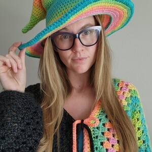 K&ouml;nnte beinhalten: Eine Frau tr&auml;gt einen Regenbogen-H&auml;kelhut und eine mehrfarbige H&auml;keljacke.