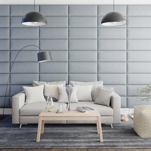 May include: A light grey sofa with white cushions sits in front of a grey wall with a light wood coffee table in front of it. There are two black pendant lights hanging from the ceiling.