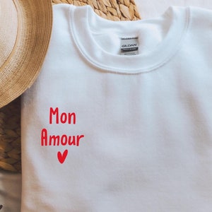 May include: White sweatshirt with red lettering that says "Mon Amour" with a small red heart.