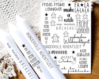 Op de afbeelding: Drie witte kaarsen met zwarte tekst en illustraties van peperkoekmannetjes. De tekst op de kaarsen luidt "Wundervolle Adventszeit" en "aus meiner Bäckerei". De achtergrond toont een witte kaart met zwarte tekst en peperkoekmannetjes-illustraties. De tekst op de kaart luidt "Friede. Freude Lebkuchen make LA-LA-LA", "a wish", "aus meiner Bäckerei", "FROHE WEIHNACHTEN", "zauberschöne Weihnachtszeit", "WUNDERVOLLE ADVENTSZEIT", "X-MAAAAAAS", "STATT Sacken", "Kein Glühwein ist auch keine Lösung", en "oh du fröhliche".