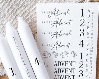 May include: Four white candles with numbers 1 through 4 printed on them. The candles are for an Advent calendar. A sheet of paper with the words "ERSTER Advent", "ZWEITER Advent", "DRITTER Advent", and "VIERTE Advent" printed on it. The paper also has a list of letters A through R with numbers 1 through 24 next to them.