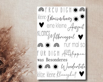 May include: A white card with black text and illustrations. The text reads "FRCU DIGH", "kleine Überraschung", "eine kleine Auszeit", "KLEINES Mitbringsel", "nur mal so", "FÜR DICH", "was Besonderes", "Wundertate", "klitze kleine Kleinigkut". The illustrations include rainbows, suns, and hearts.