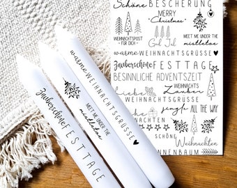 May include: Three white candles with black text that reads "warme Weihnachtsgrüsse", "Zauberschöne FESTTAGE", and "MEET ME UNDER THE mistletoe". The candles are arranged vertically with the text facing the viewer. The background is a white fuzzy surface.
