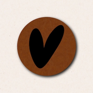 Puede incluir: Un posavasos de cuero marrón con una forma de corazón negro en el centro.