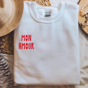May include: White sweatshirt with the phrase "Mon Amour" in red lettering with small hearts.